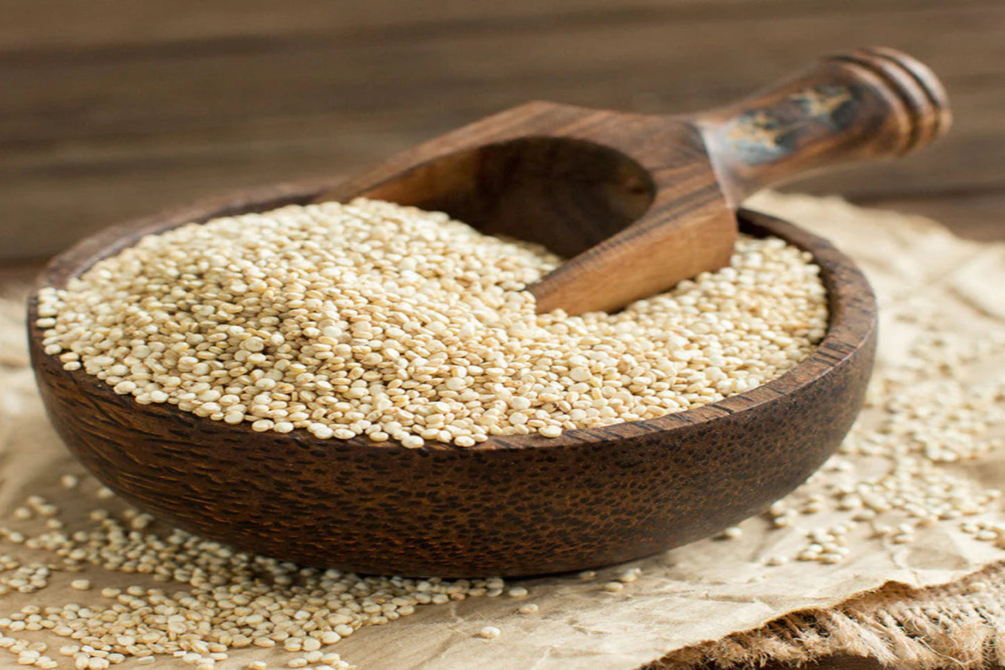Wooden scoop filled with quinoa in a wooden bowl on a rustic background