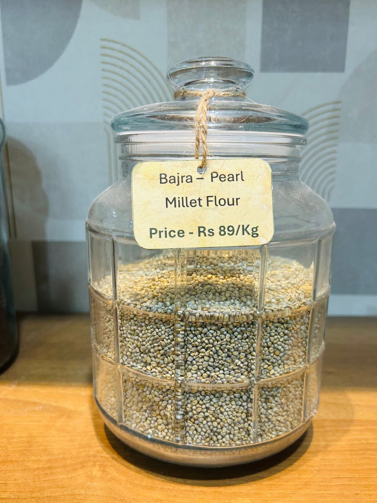 Glass jar filled with Bajra Pearl Millet Flour on a wooden surface
